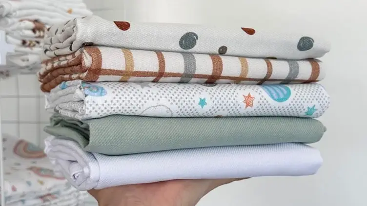 Pilha de paninhos de boca de bebê dobrados com estampas variadas em uma mão