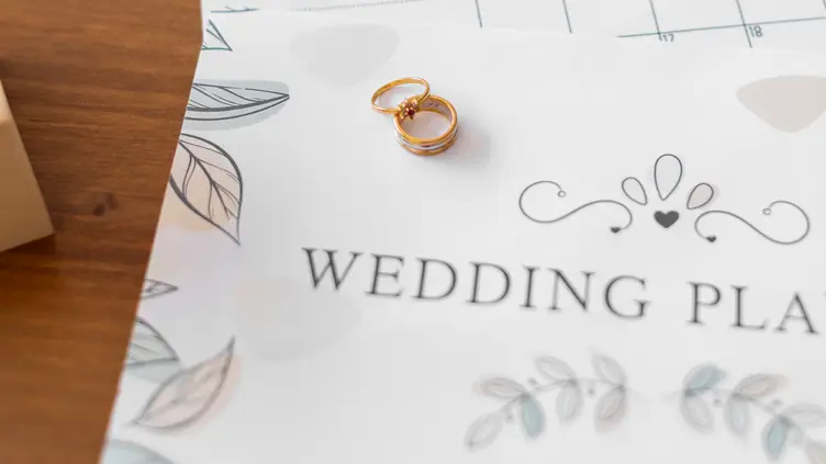 Duas alianças de casamento sobre um planejador com a frase Wedding Planner escrita em uma mesa de madeira
