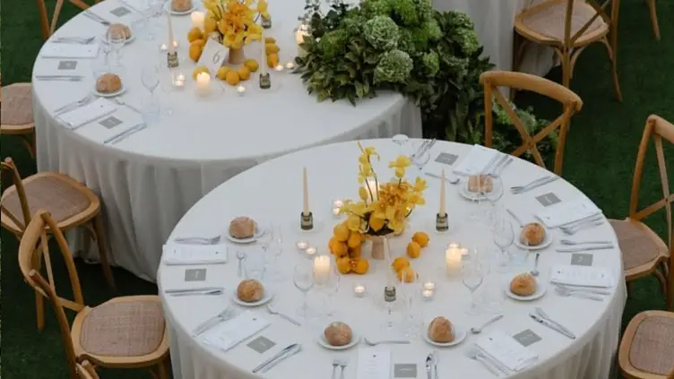 Mesas redondas de recepção de casamento decoradas com arranjos de flores amarelas e limões sicilianos em gramado