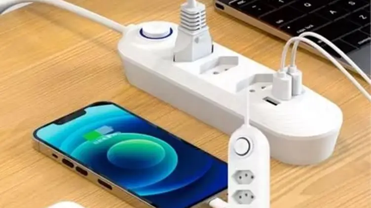 Filtro de linha branco com tomadas e portas USB conectado a um smartphone sobre uma mesa de madeira